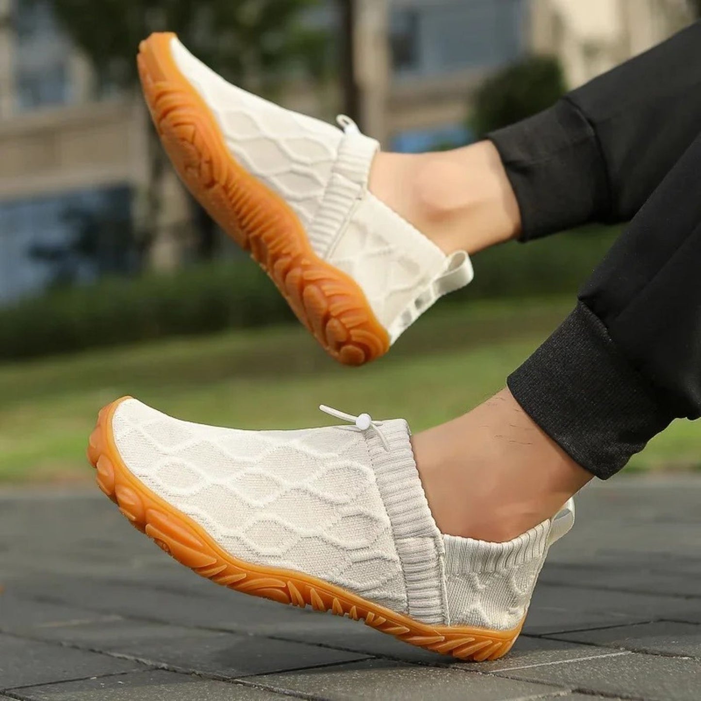 White slip-on shoes with orange soles worn outdoors, paired with black pants.