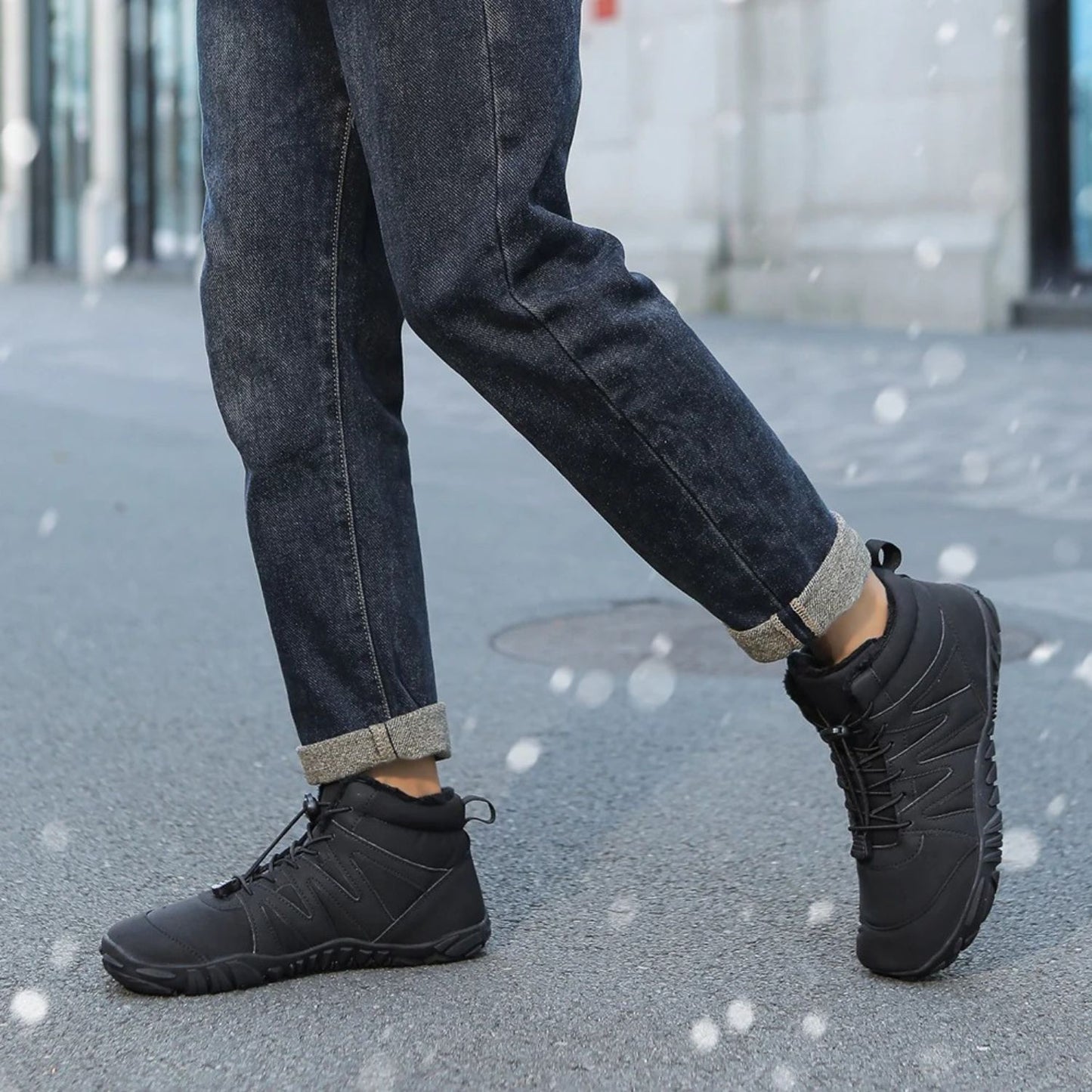 Black winter boots worn with cuffed jeans, walking outdoors on pavement.