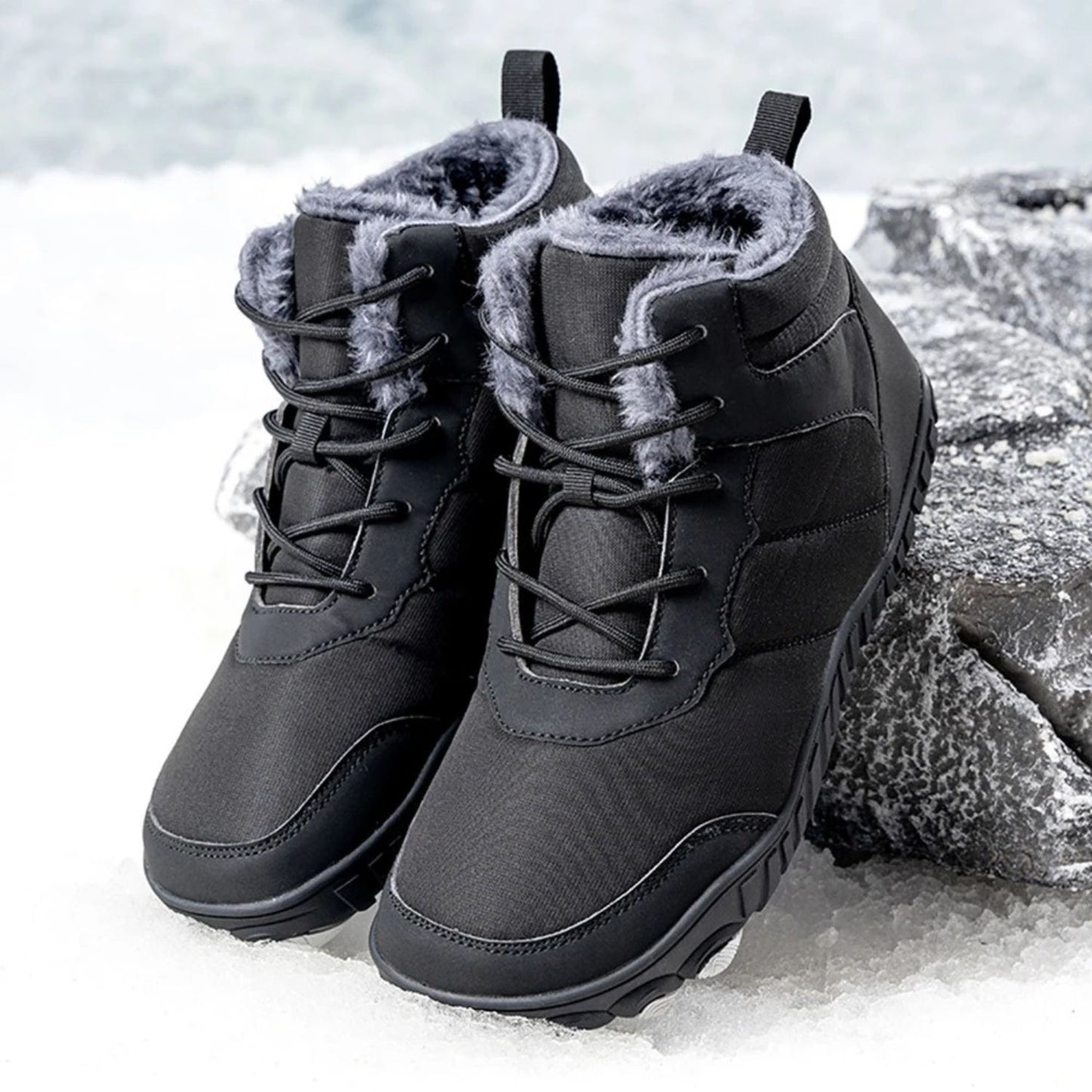 Pair of black winter boots with fleece lining displayed on snow-covered rock.
