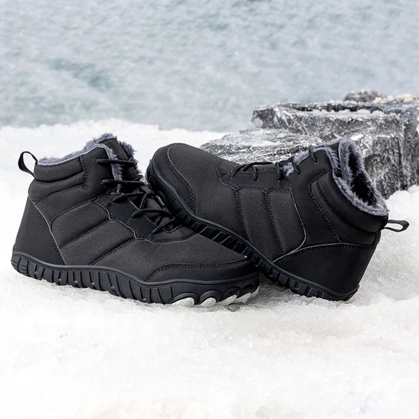 Black fleece-lined winter boots placed in snow with icy water background.