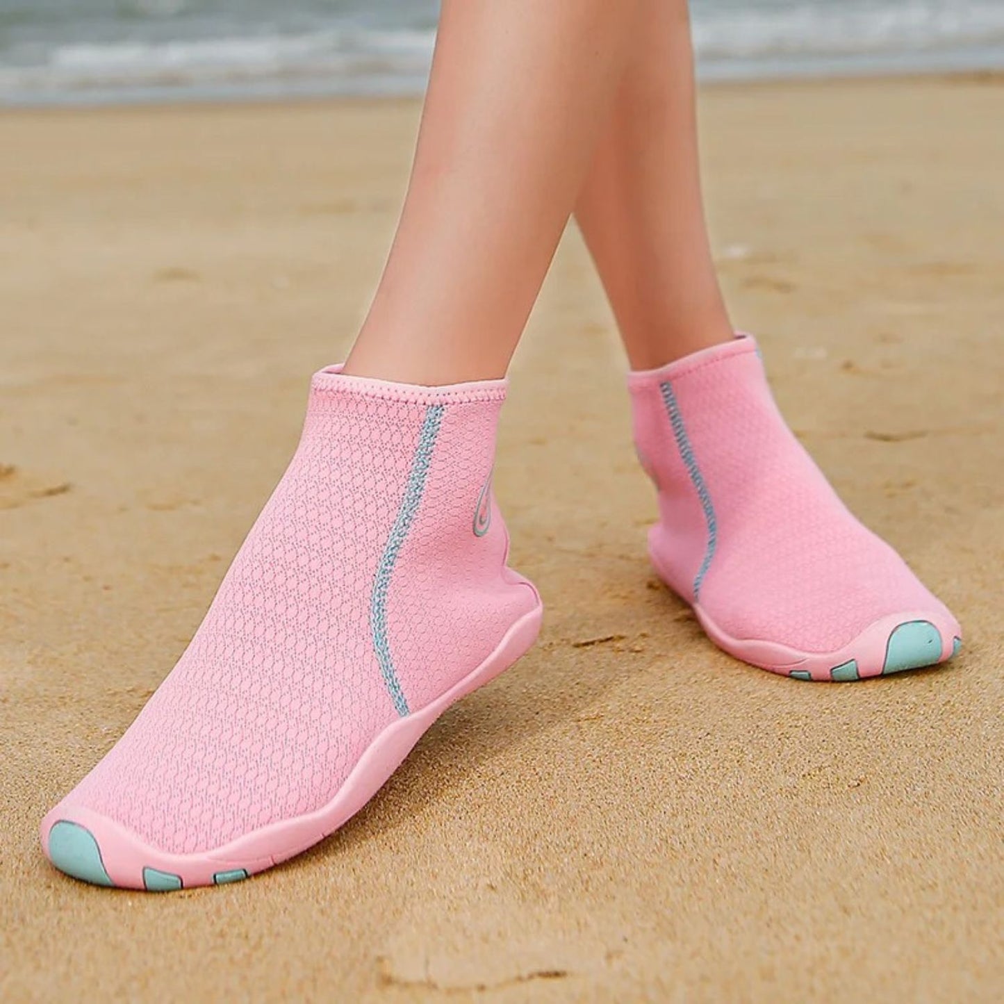 Pink zip-up water shoes worn on beach, shown from front with ankles exposed.