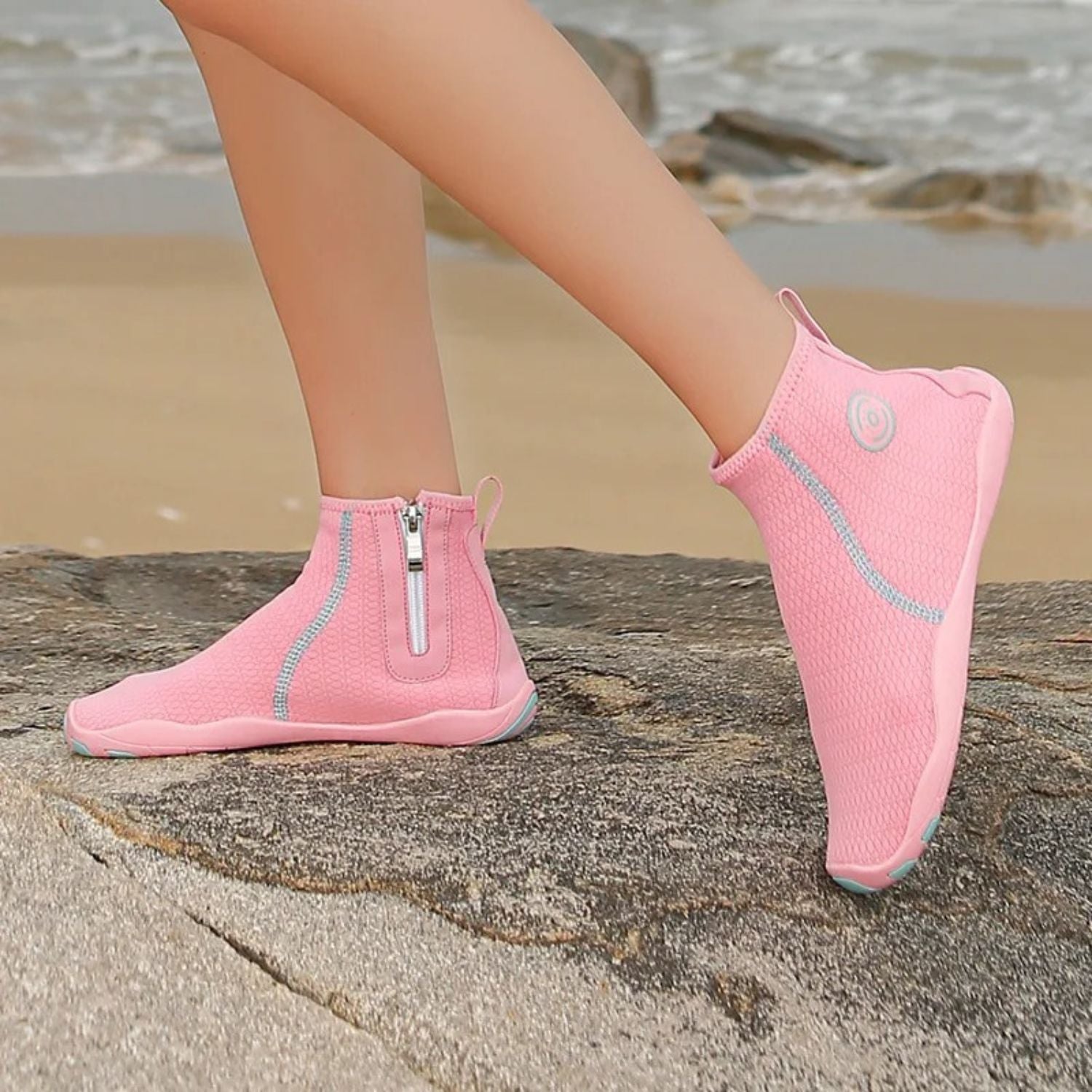Person wearing pink high-ankle water shoes with zipper, standing on sand.