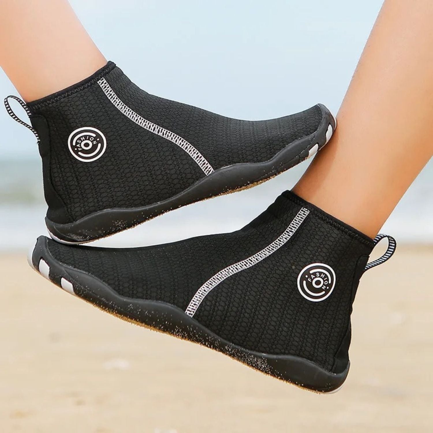 Back view of black zip-up water shoes with circular logo and light sole, worn on sand.