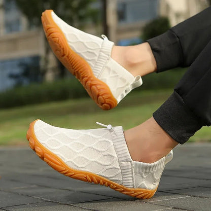 White slip-on shoes with orange soles worn outdoors, paired with black pants.