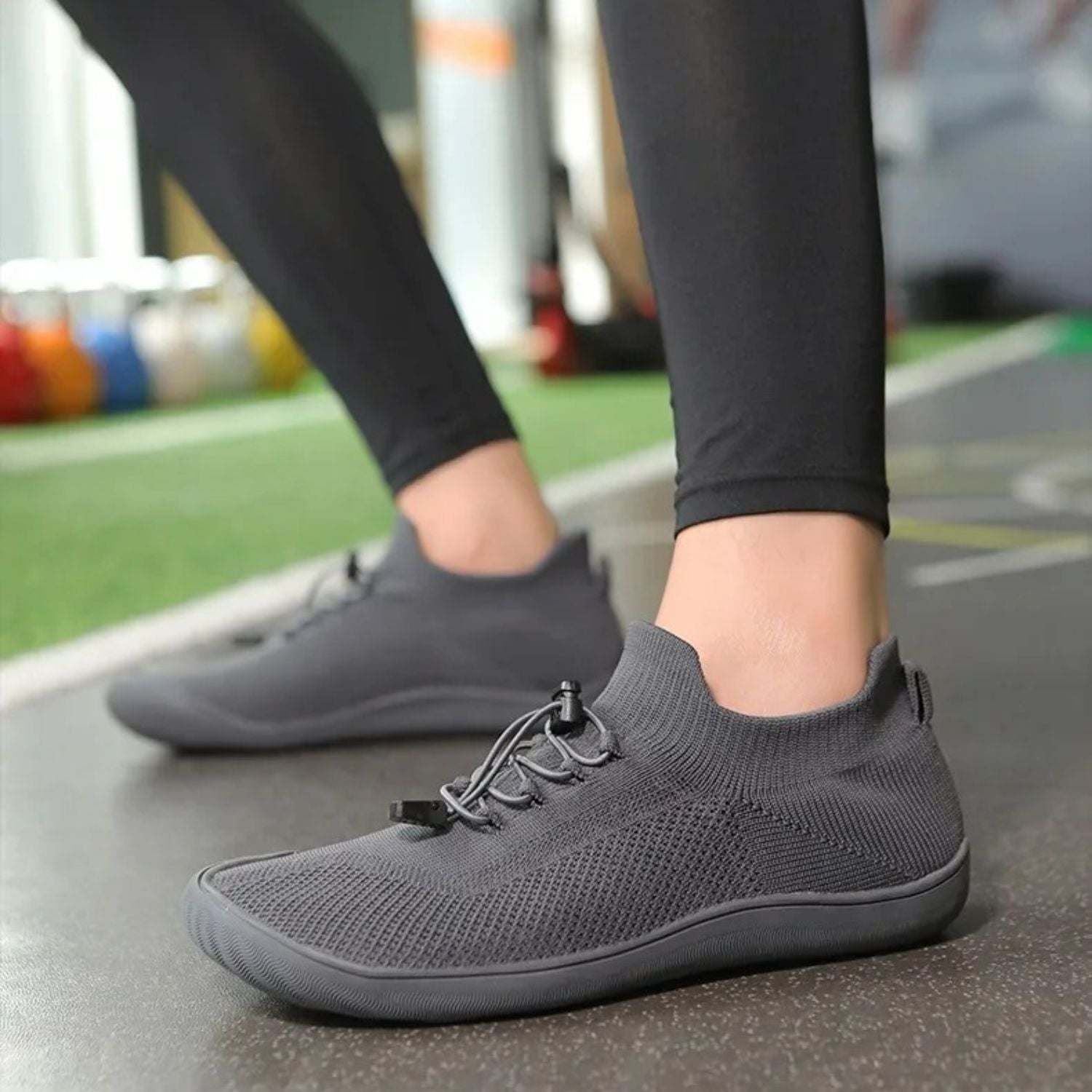 Gray barefoot sneakers worn with leggings, walking across fitness area.