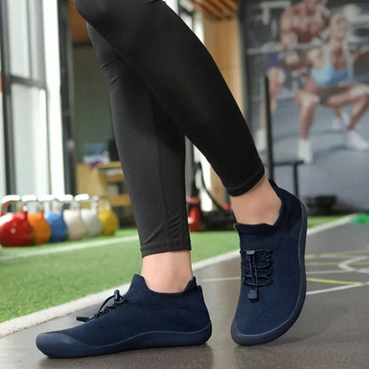 Person wearing navy barefoot sneakers on gym floor with kettlebells in background.
