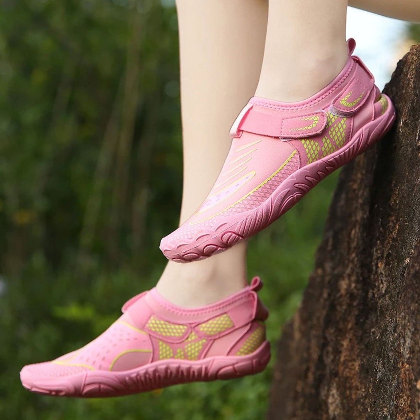 Person wearing pink water shoes with green sole, stepping on tree outdoors.
