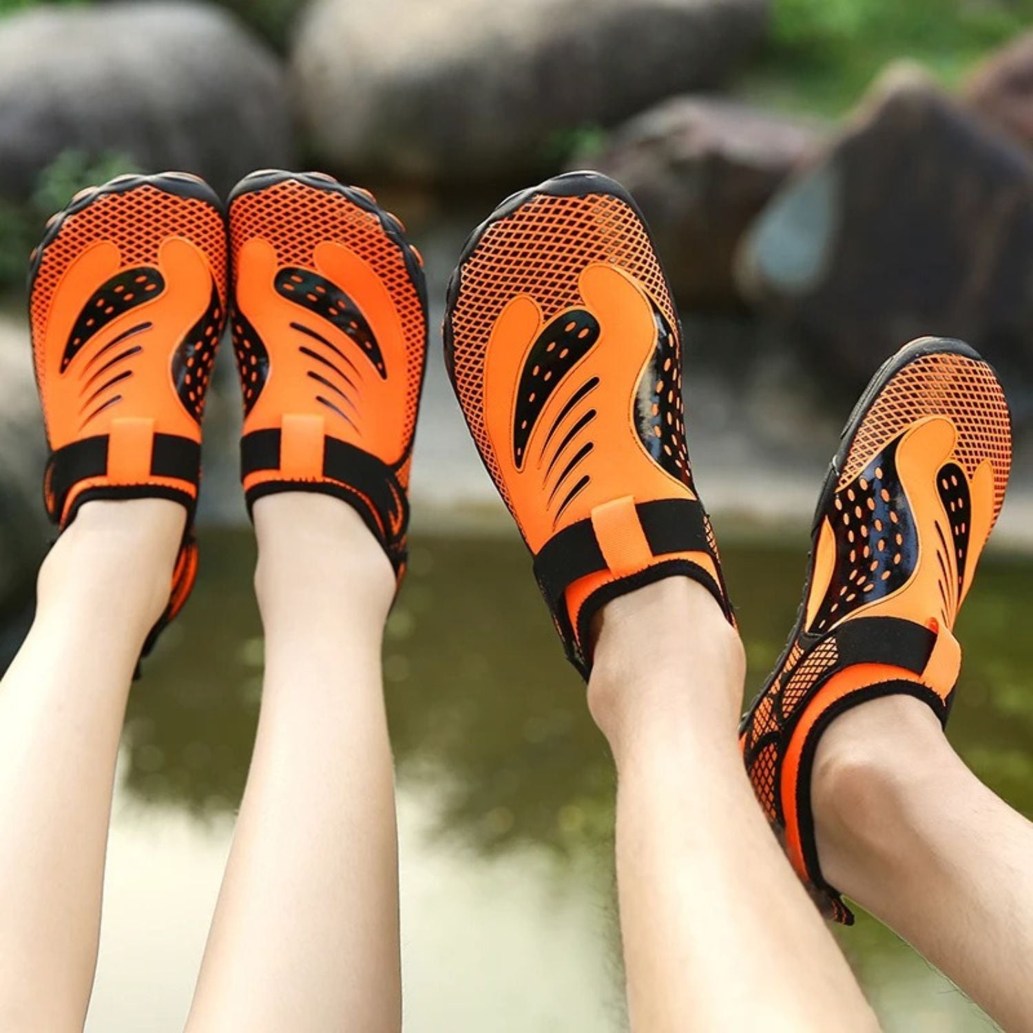 Two people wearing orange water shoes, feet extended together outdoors.