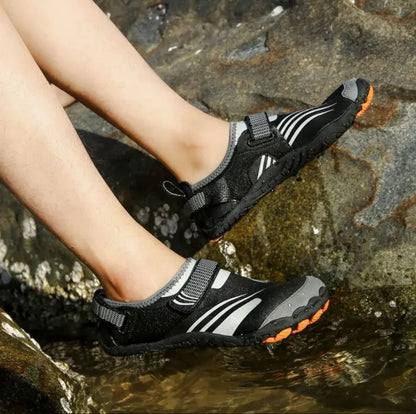 Black and orange water shoes worn in a rocky stream for outdoor activity.