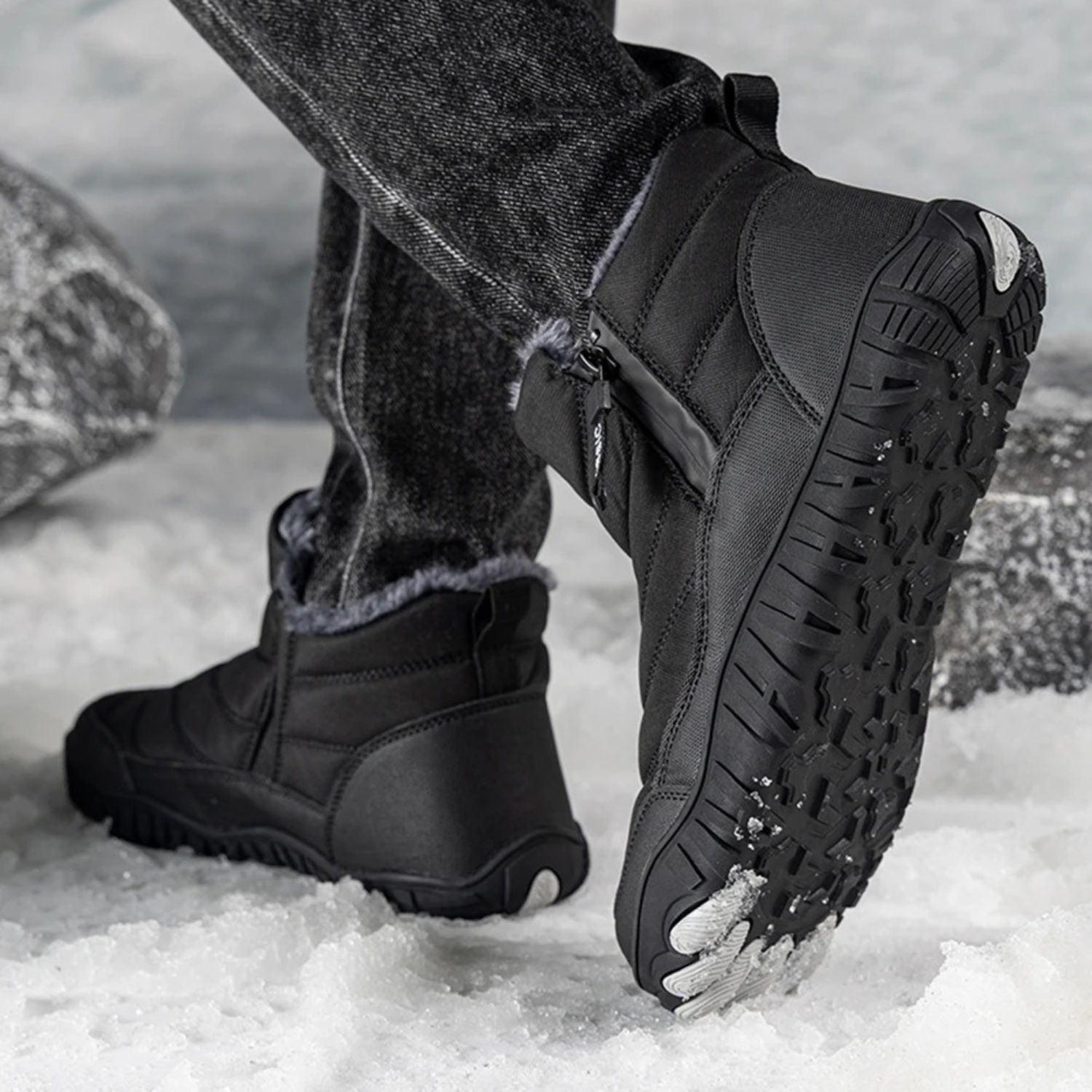 Person wearing black ankle boots with thick traction sole, walking in snowy setting.