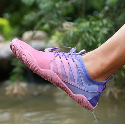 Person wearing lavender and pink water shoes, stepping into shallow water.