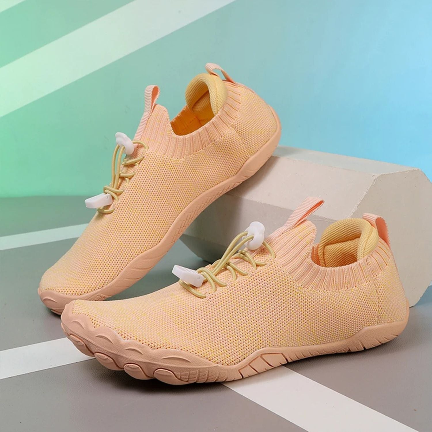 Beige knit barefoot shoes with orange interior lining, displayed against pastel background.